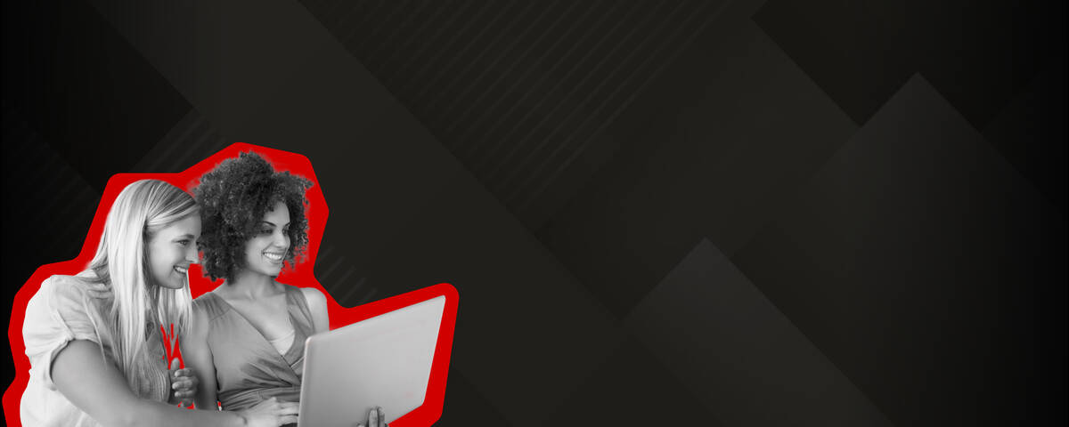 Zwei Frauen lächeln während sie auf den Laptop schauen.