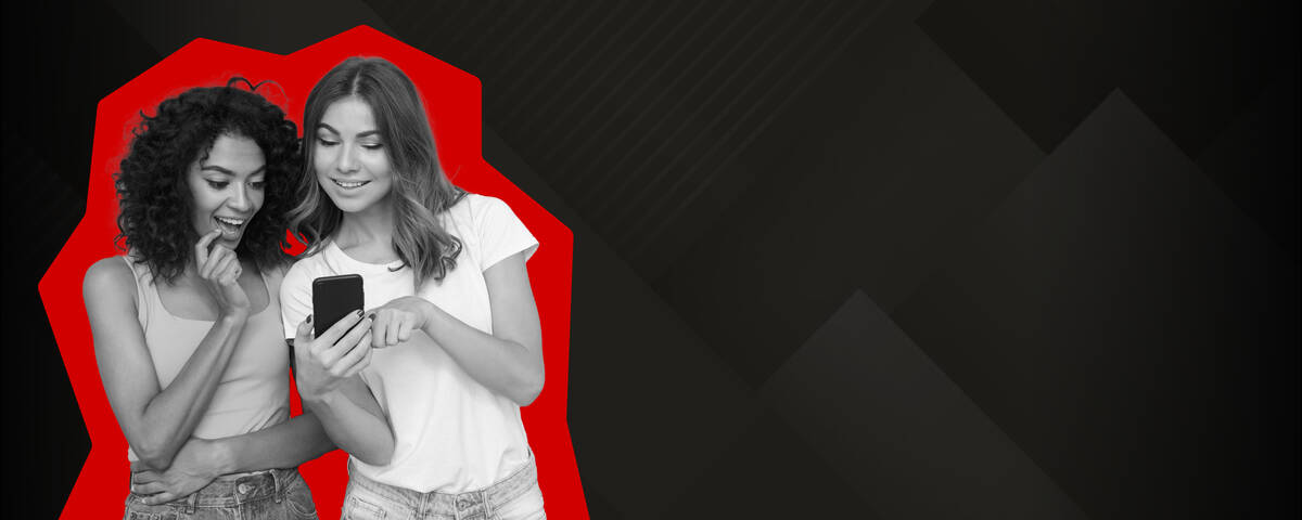 Zwei Frauen stehen lächelnd nebeneinander und schauen auf ihr Handy