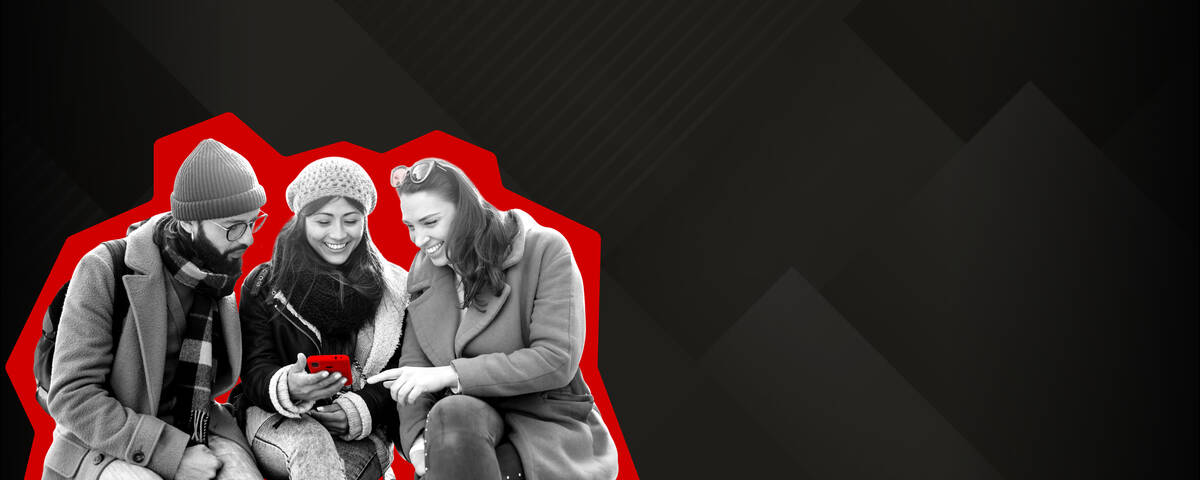 Zwei Frauen stehen lächelnd nebeneinander und schauen auf ihr Handy